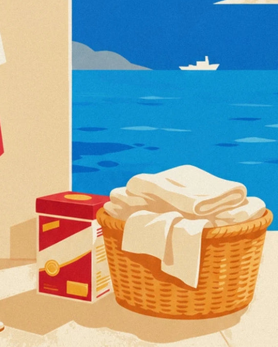 Panier en osier plein de linge blanc et boîte de lessive rouge, face à la mer et son bateau